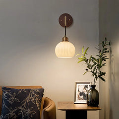 A living room scene with a walnut wood wall sconce featuring a frosted glass shade, illuminating the area above a framed picture.