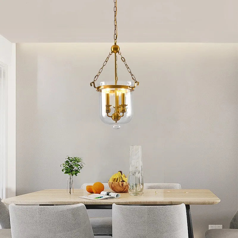 Polished copper and clear glass drum pendant light installed over a dining table
