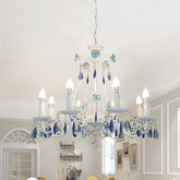 White metal chandelier with blue floral accents and blue crystal drops, illuminated and hanging from a white ceiling in a dining room setting.