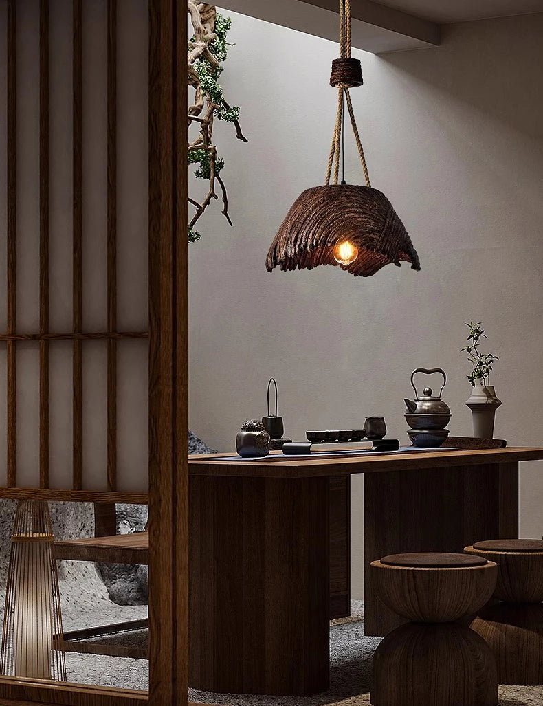 Rustic pendant light hanging above a wooden table with tea-making items in a dimly lit room.