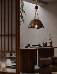 Rustic pendant light hanging above a wooden table with tea-making items in a dimly lit room.