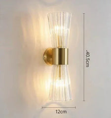 Wall-mounted light fixture with gold finish and clear glass shade on a white background