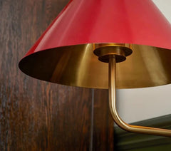 Close-up of a lamp with a red shade and gold base against a wooden wall.