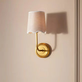 Wall-mounted lamp with a white shade and gold base on a beige wall.