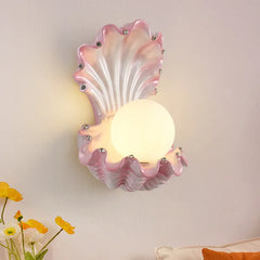 Close-up of a pink seashell wall sconce with a frosted globe light and small crystal accents, with yellow flowers in the foreground.