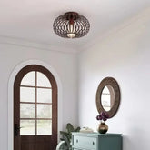 Brushed gold open cage semi-flush ceiling light mounted on a white ceiling in a hallway with a wooden arched door and a teal dresser.
