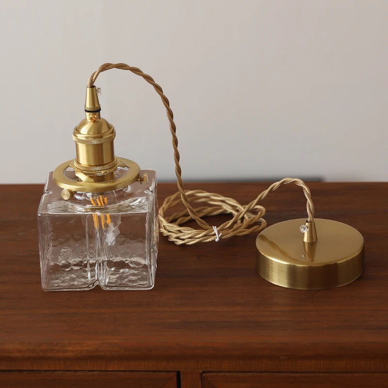A glass square pendant light fixture disassembled, showing the glass shade, brass socket, and cord.