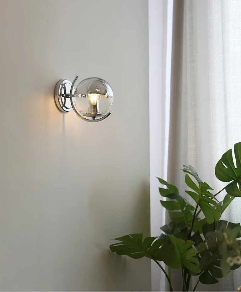 Wall-mounted light fixture on a white wall with a plant in the foreground