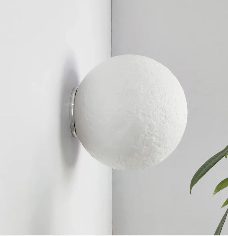 Spherical wall light fixture on a white wall with a plant in the corner