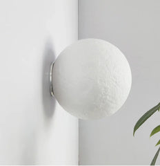 Spherical wall light fixture on a white wall with a plant in the corner