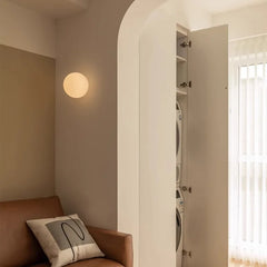 Living room with a brown sofa, round wall light, and open door revealing a laundry area.