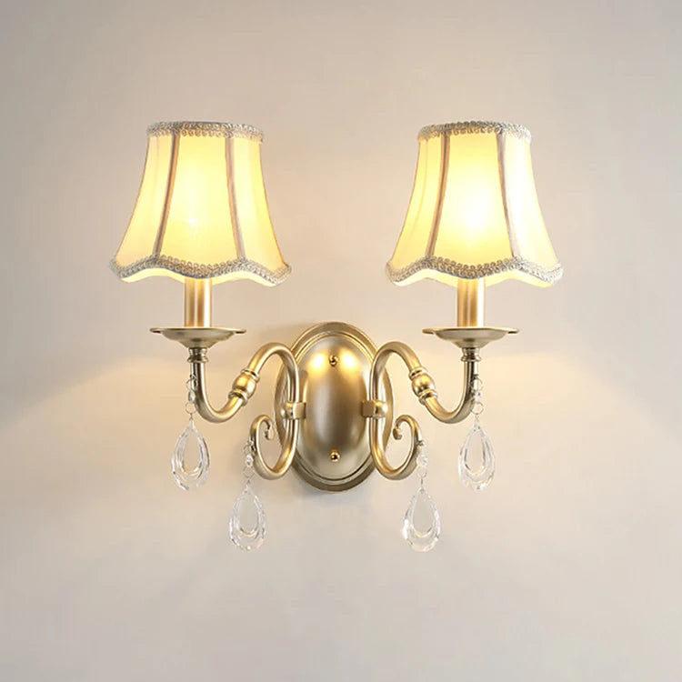 Pair of wall sconces with lampshades and crystal accents on a plain wall.
