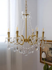 Gold chandelier with crystal accents hanging in a room with a painting and plant.