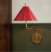 Wall-mounted lamp with red shade and gold fixture on a green wall.