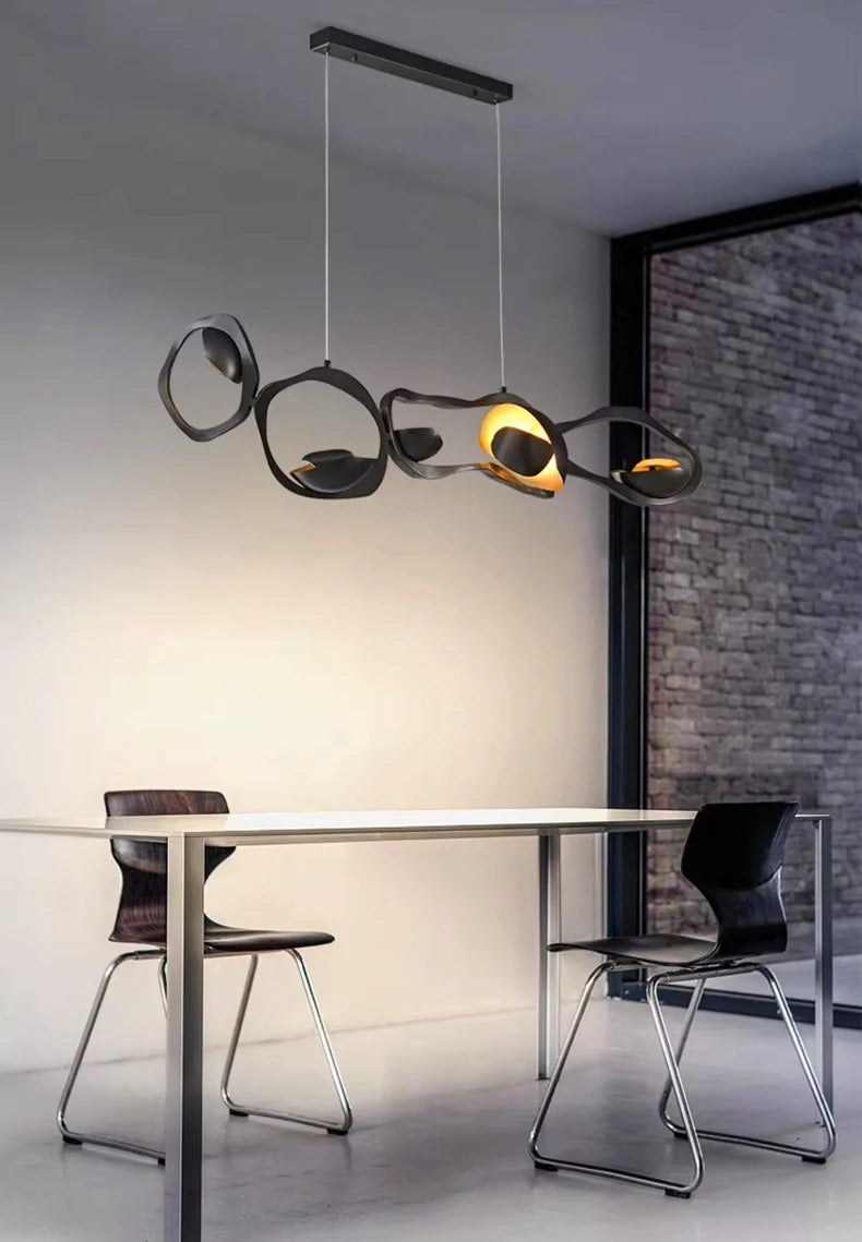Modern chandelier hanging above a dining table with chairs in a room with a brick wall.
