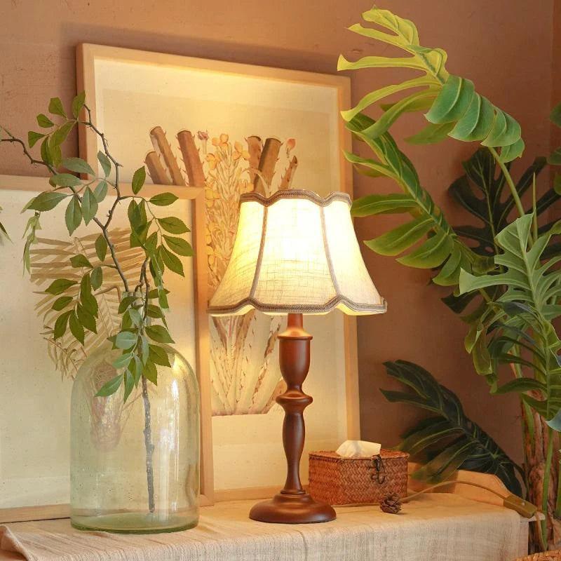 Decorative table lamp with a warm glow on a surface, surrounded by plants and a framed picture.