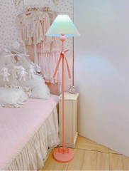 Pink floor lamp in a bedroom setting with a bed and nightstand.