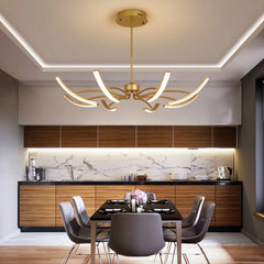 Gold chandelier with curved arms and LED lights above a dining table in a modern kitchen.