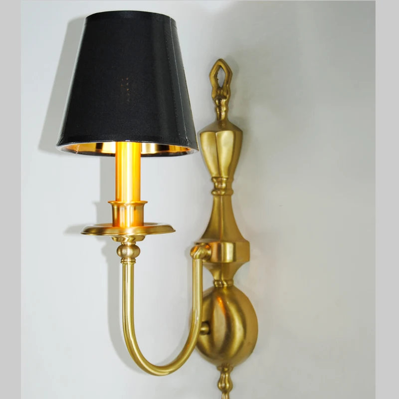 Gold wall sconce with a black lampshade on a white background