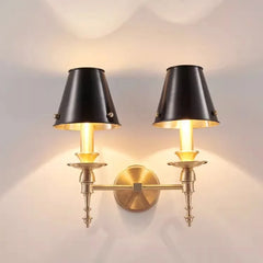 Pair of wall sconces with black lampshades and gold brackets on a light gray wall.