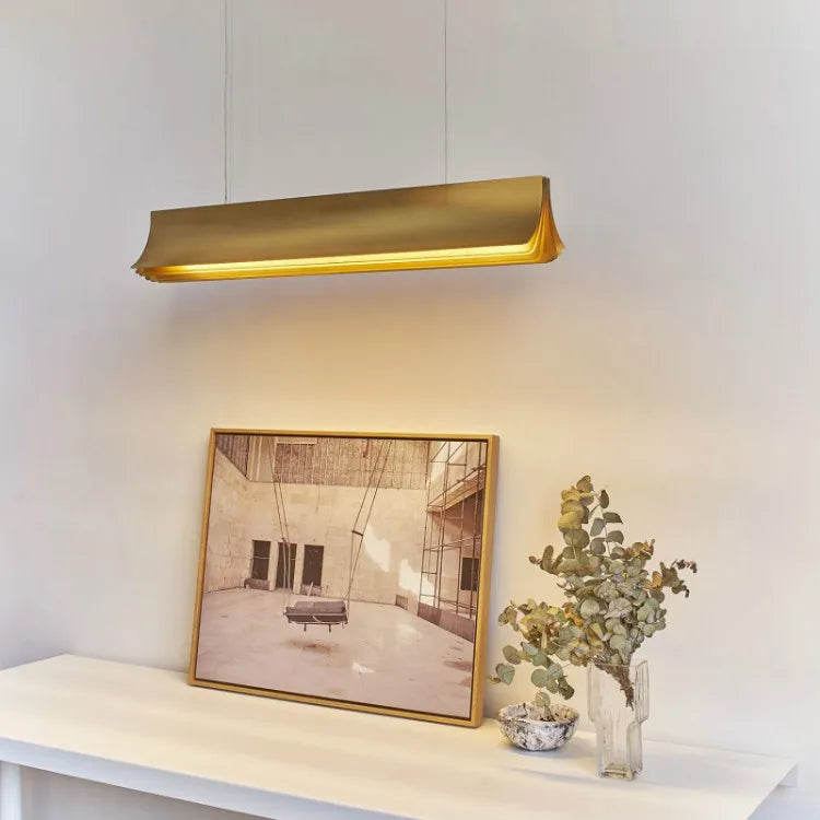 Gold pendant light fixture above a table with a framed picture and plant.