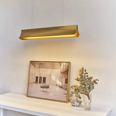 Gold pendant light fixture above a table with a framed picture and plant.