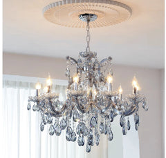 The grey metal frame of the crystal chandelier is detailed with ornate carvings and suspended teardrop crystals.