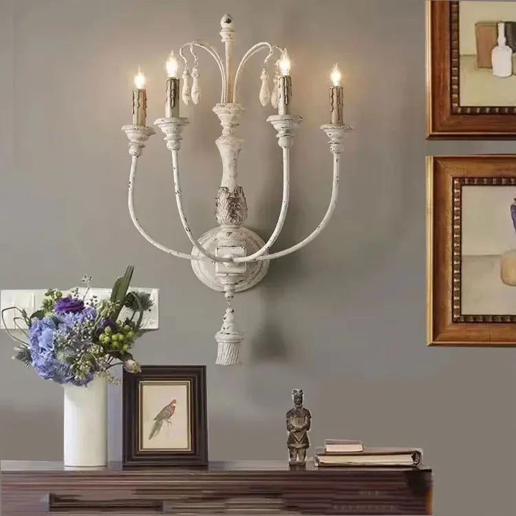 Decorative wall sconce with candles on a wall with framed pictures and a vase of flowers.