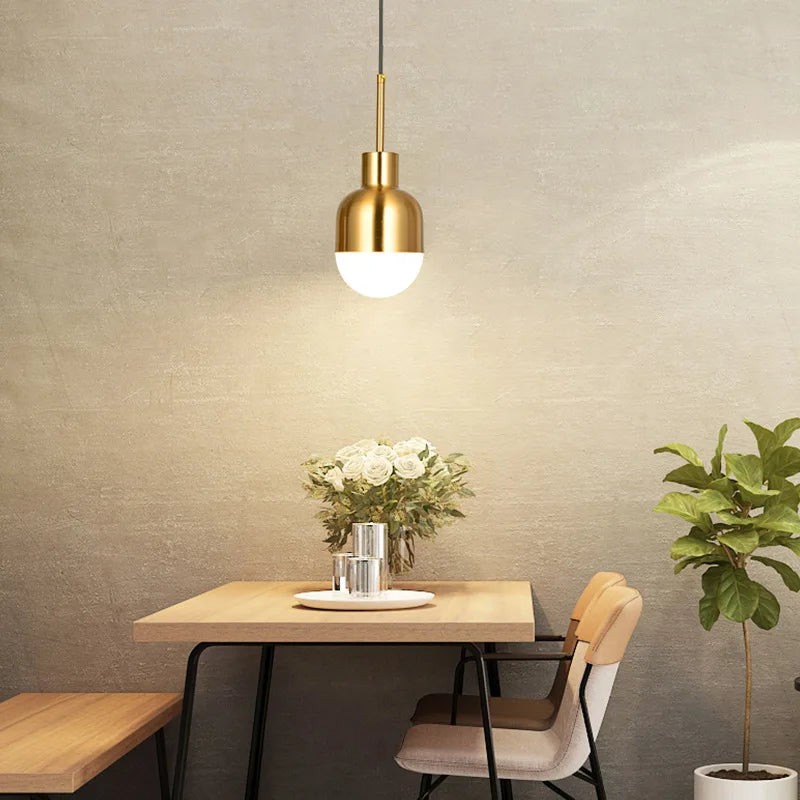 A gold metal dome pendant light suspended over a wooden dining table with chairs.