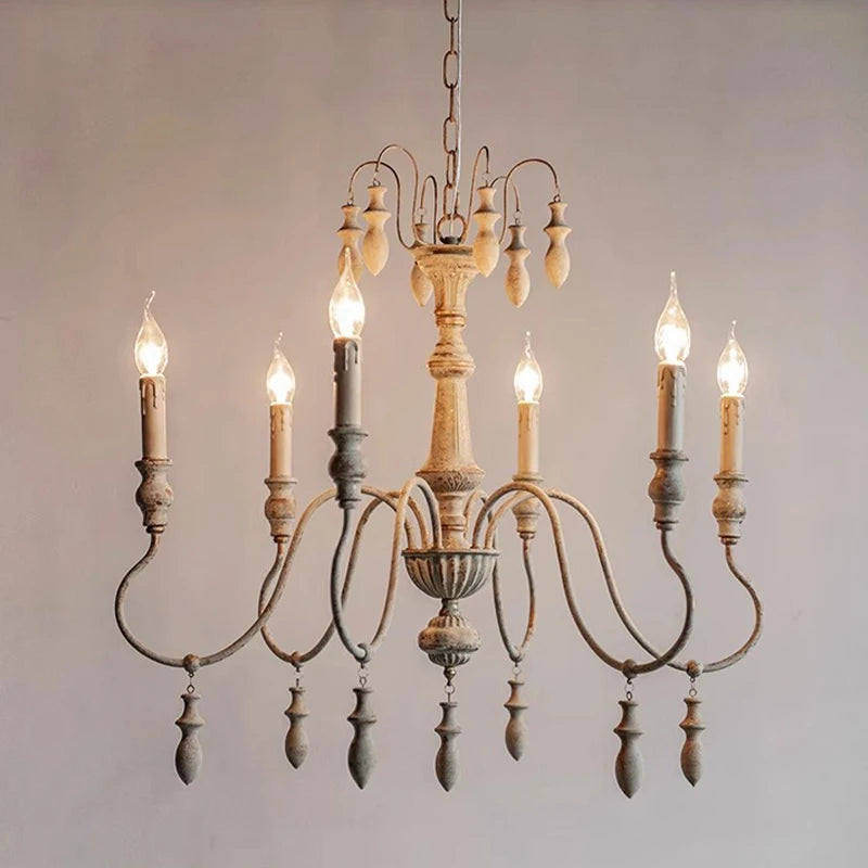 Side view of a distressed white iron chandelier featuring multiple candle-style lights and decorative wooden drops.
