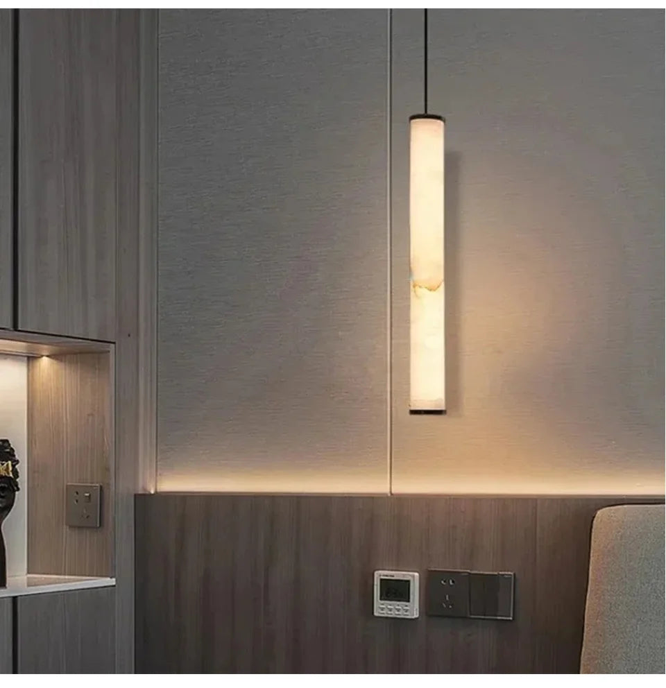A marble cylinder pendant light with natural stone detail illuminated above a wooden headboard.
