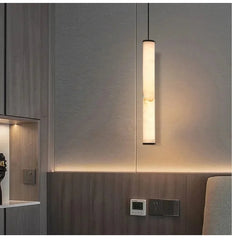 A marble cylinder pendant light with natural stone detail illuminated above a wooden headboard.