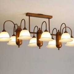 A product image of a brushed gold linear chandelier with multiple frosted glass bell-shaped shades, mounted on a white ceiling.