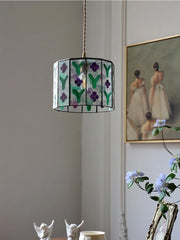 Decorative pendant light with floral design hanging in a room with a painting and plants.