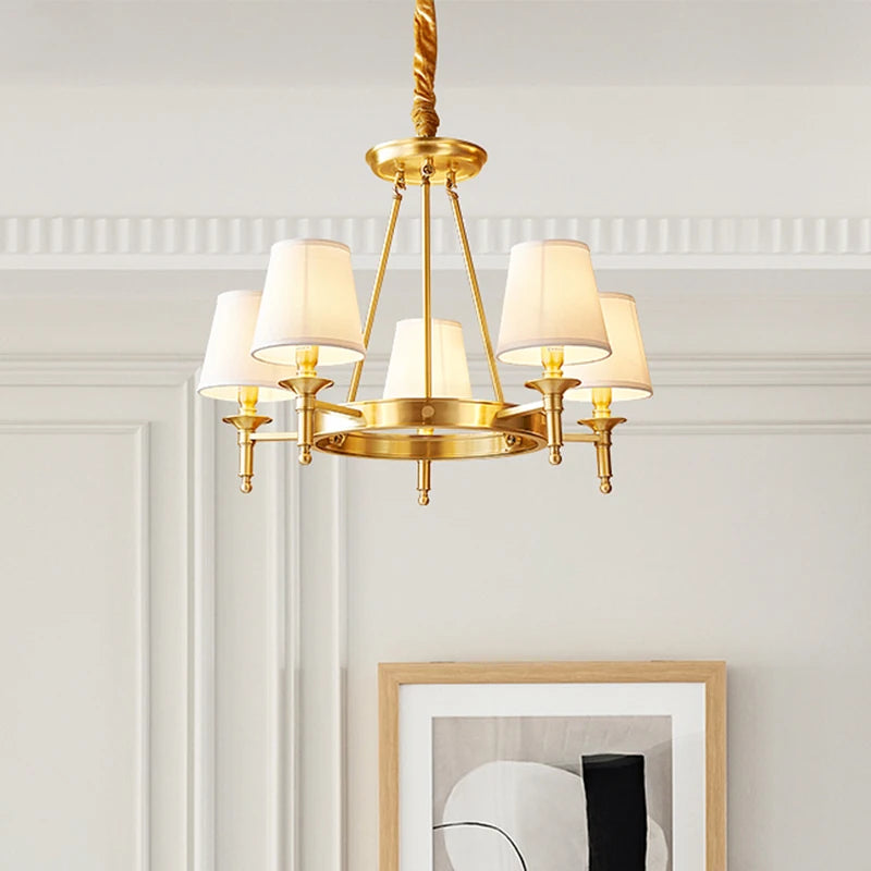 Polished copper ring chandelier with five white fabric drum shades, angled view.