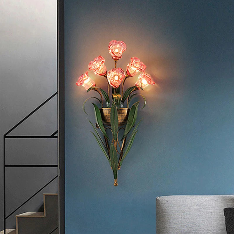 Pink floral wall sconce with clear glass flower shades and green leaf accents mounted on a blue wall.