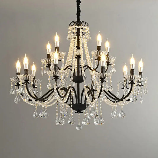 Black wrought iron candelabra chandelier with multiple arms adorned with clear crystal prisms and white pearl bead strands hanging against a gray backdrop.