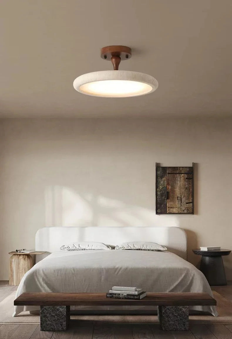 A bedroom with a contemporary aesthetic, centered around a stone and wood ceiling light fixture, with minimalist decor and natural light.