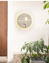 Round natural stone wall sconce with carved staircase and archway, mounted on a white wall next to a planter and wooden door.