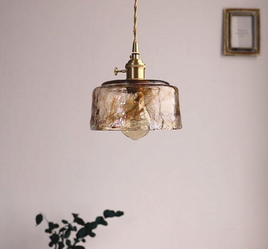 Pendant light with glass shade and brass fixture hanging in a room.