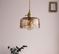 Pendant light with glass shade and brass fixture hanging in a room.
