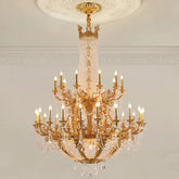 Close-up of a gold tiered chandelier with crystal accents and candelabra-style arms, illuminated against a white ceiling and wall.