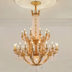 Close-up of a gold tiered chandelier with crystal accents and candelabra-style arms, illuminated against a white ceiling and wall.