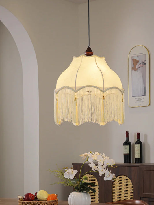 Cream fabric scalloped pendant light with gold tassels hanging above a dining table, showing the fringed detail.