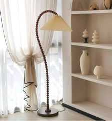 Floor lamp with a wooden base and beige shade next to a white bookshelf with decorative items.
