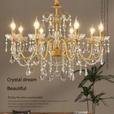 A close-up view of a luxurious gold chandelier adorned with numerous clear crystals and pearls, with warm light emanating from candle-shaped bulbs.
