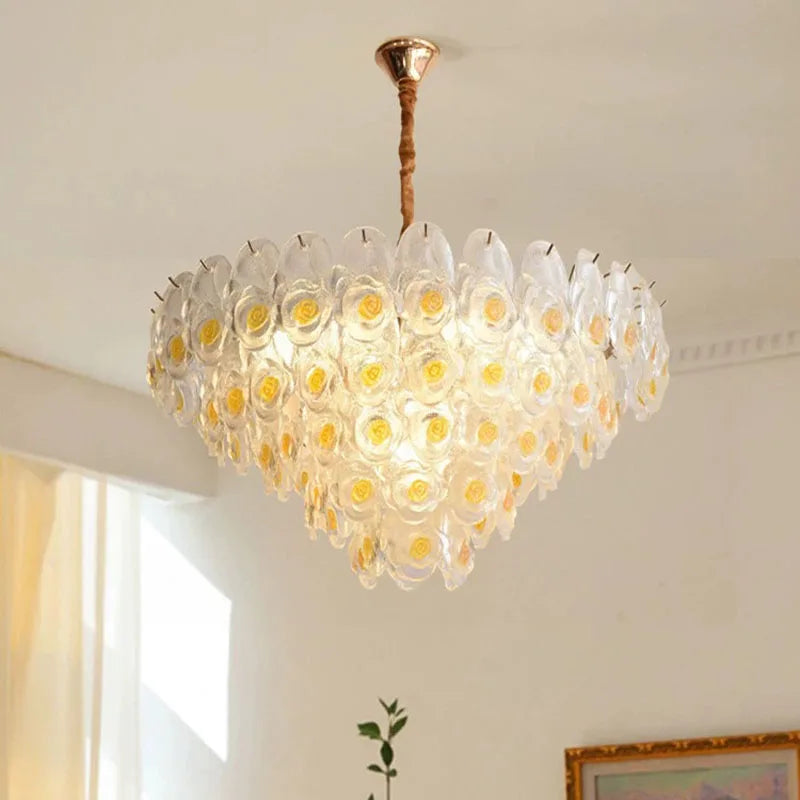 Brushed gold chandelier with clear glass and yellow rose accents, illuminated.