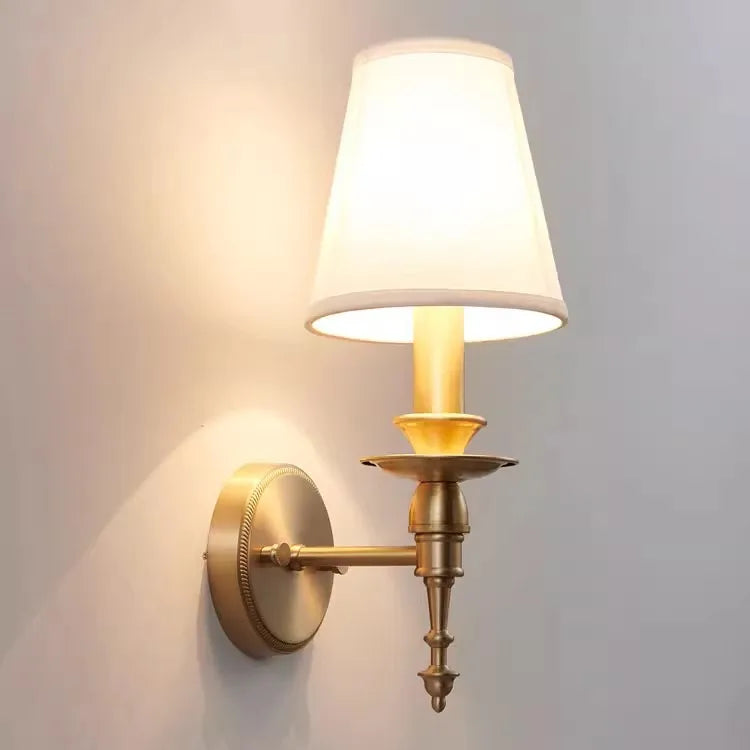 Wall-mounted lamp with white shade and brass base on a light gray wall