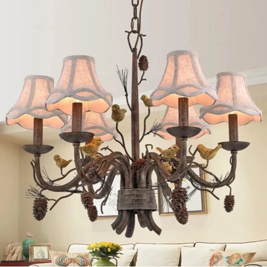 Gold floral-themed chandelier with bird and pine cone accents, featuring fabric shades and a rustic finish, suspended in a living room setting.