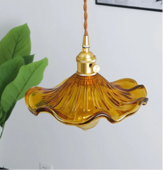 Amber glass pendant light with gold fixture against a white wall.